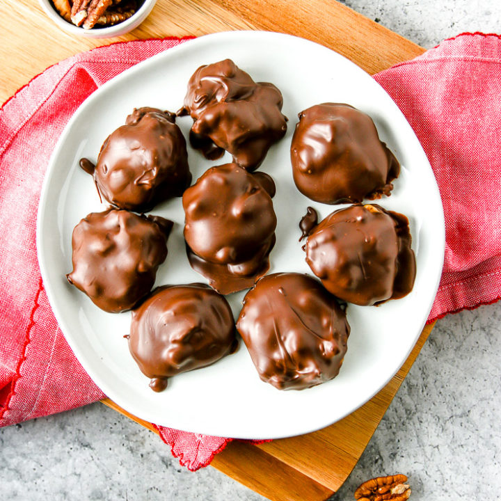 an overhead shot of a white plate with chocolate covered pecan turtles with pecans around the plate