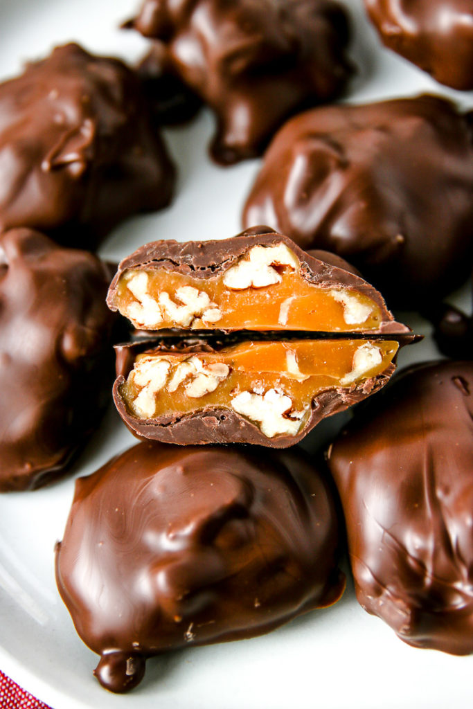 a chocolate covered pecan turtle cut in half showing the caramel and pecans inside