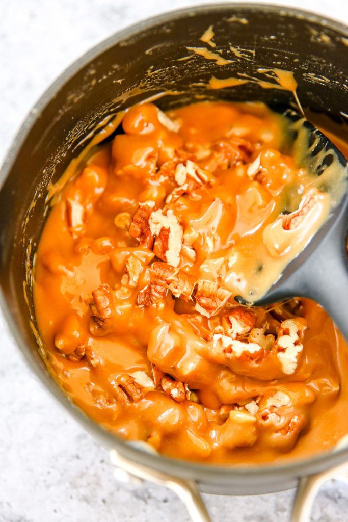 a saucepan of melted caramel and chopped pecans being stirred