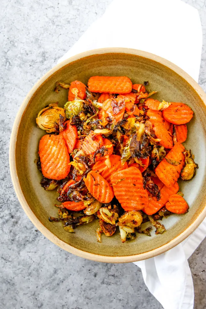 an earthy green bowl on a white napkin with a scoop of roasted brussels sprouts and carrots
