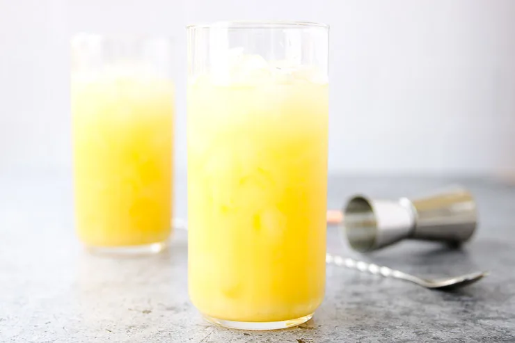 one in focus screwdriver cocktail in a highball glass with one behind it and a jigger and stirrer