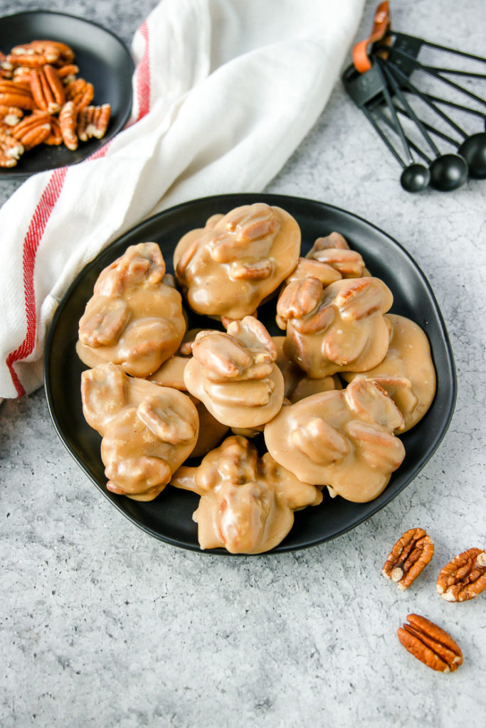 a black plate full of pecan pralines with pecans spread next to it