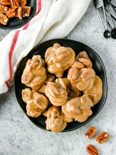 an overhead shot of pecan pralines on a black plate next to a white napkin