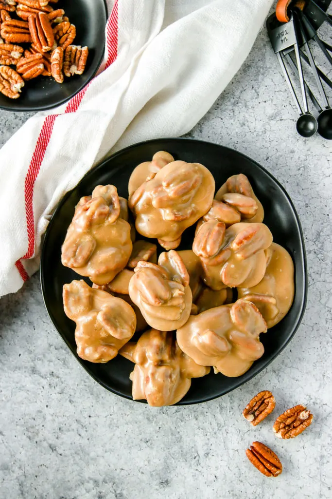 an overhead shot of pecan pralines on a black plate next to a white napkin