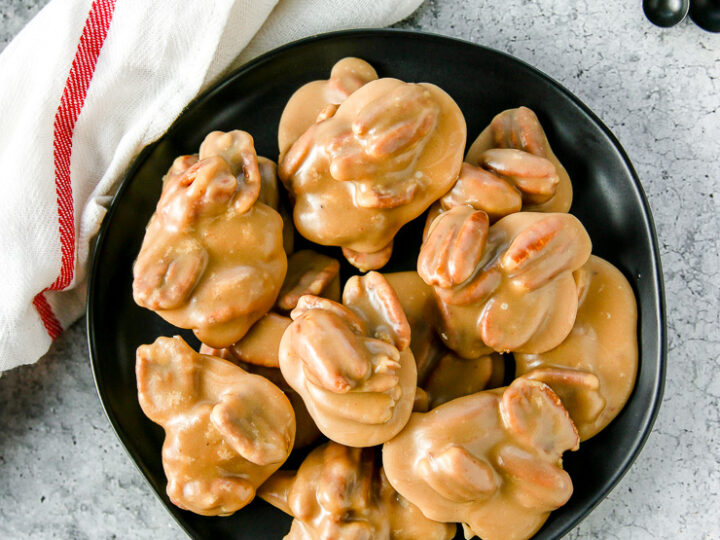 an overhead shot of pecan pralines on a black plate next to a white napkin