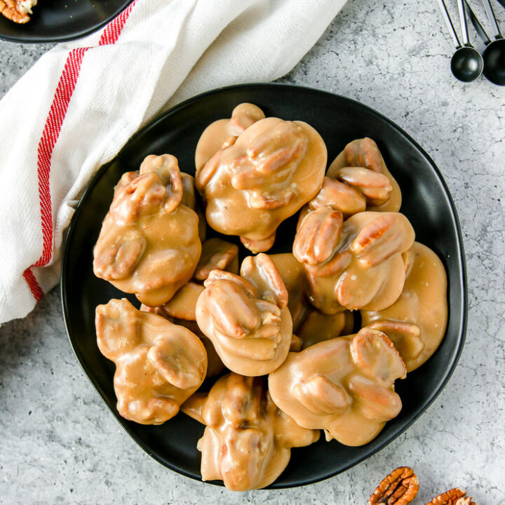 an overhead shot of pecan pralines on a black plate next to a white napkin