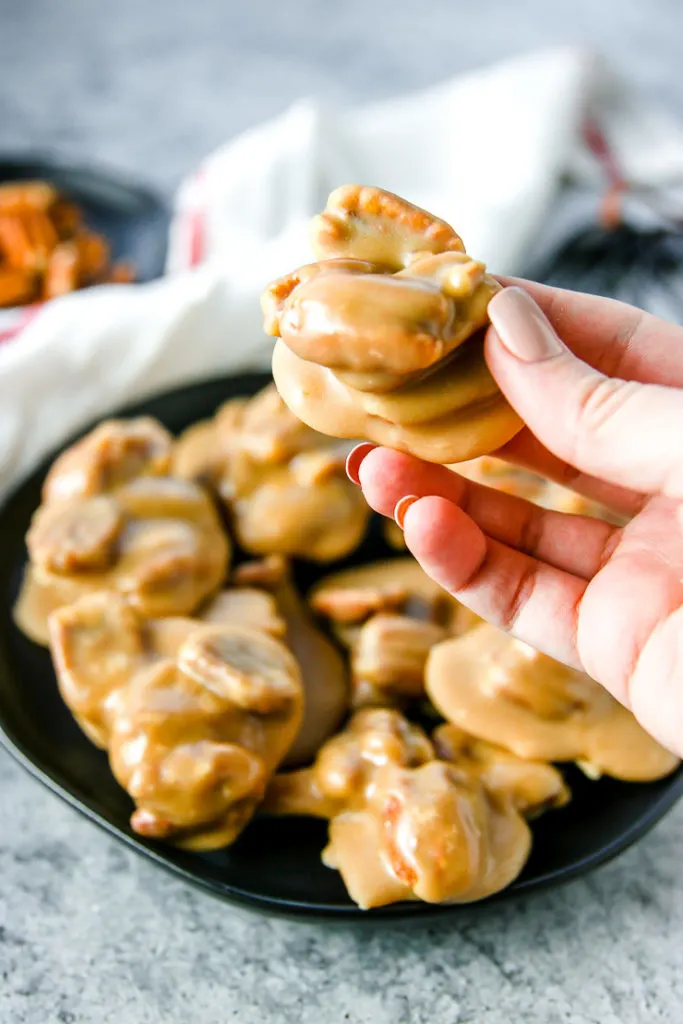 a hand holding a pecan praline over the plate