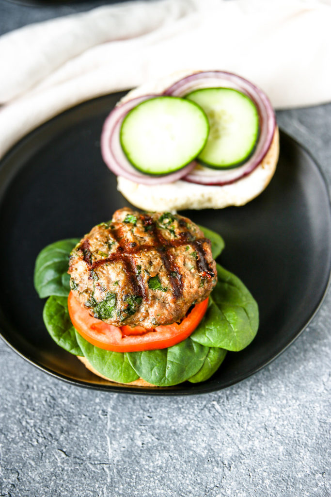 an open bun with cucumber and red onion and the spinach feta turkey burger on the other side