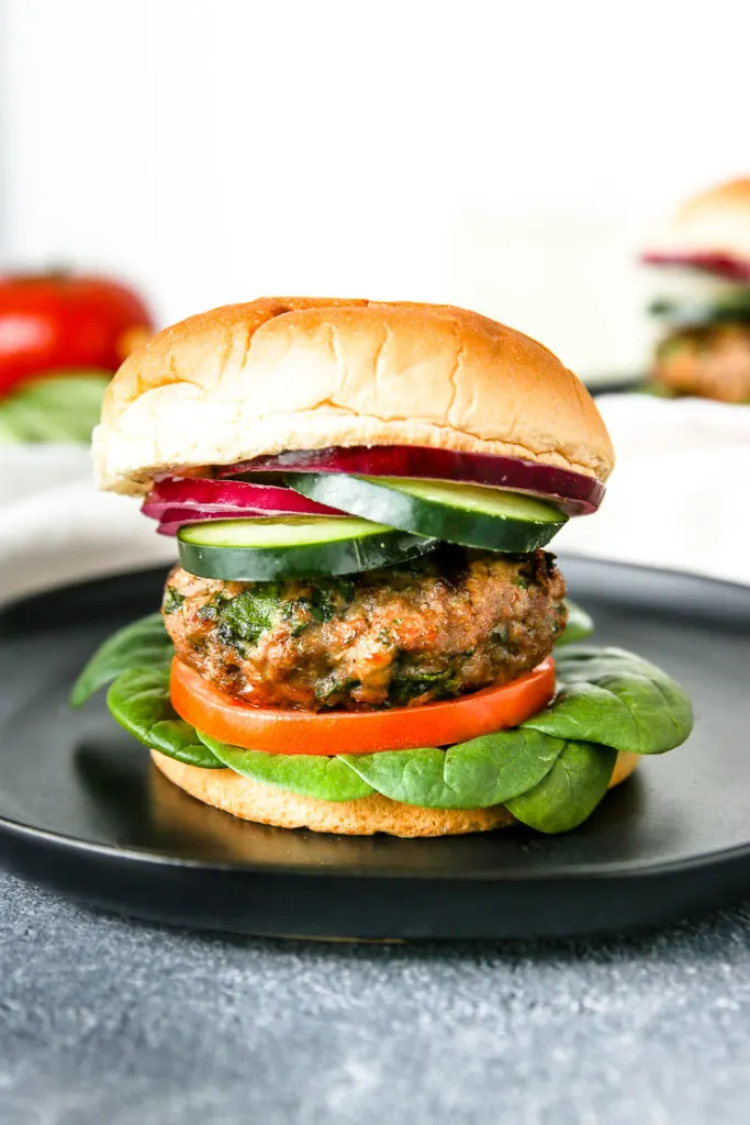 layers of spinach, tomato, a spinach feta turkey burger, cucumber, and red onion on the bun