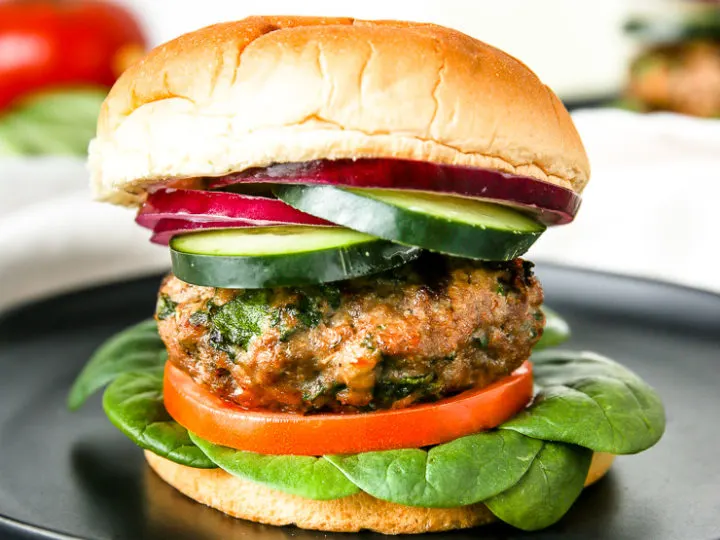 layers of spinach, tomato, a spinach feta turkey burger, cucumber, and red onion on the bun