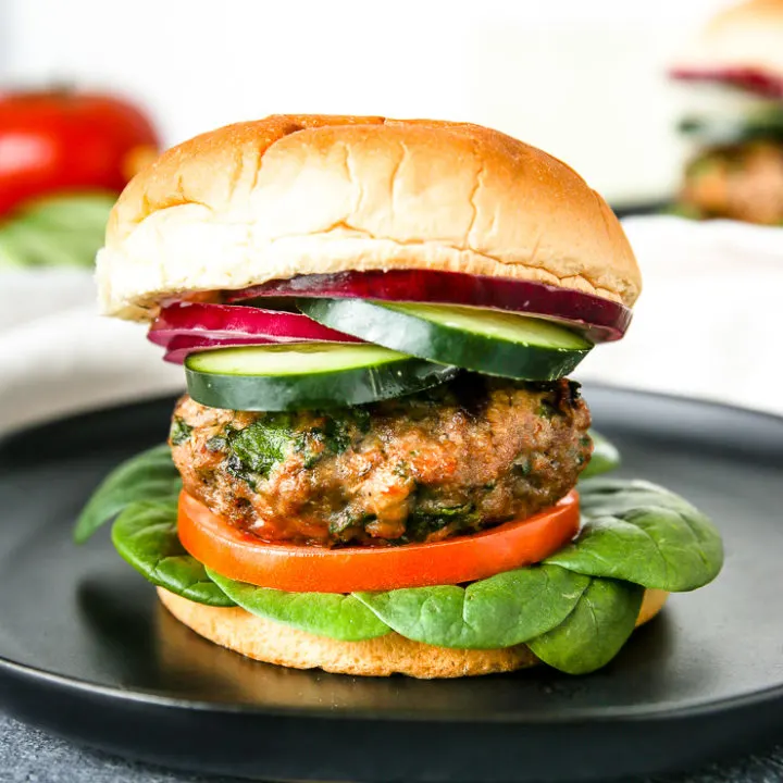 layers of spinach, tomato, a spinach feta turkey burger, cucumber, and red onion on the bun