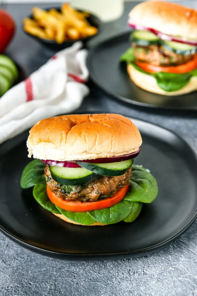 a spinach feta turkey burger on a black plate with another in the background