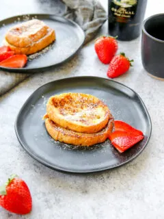 two plates of baileys french toast with strawberries, a mug of coffee, and bottle of baileys