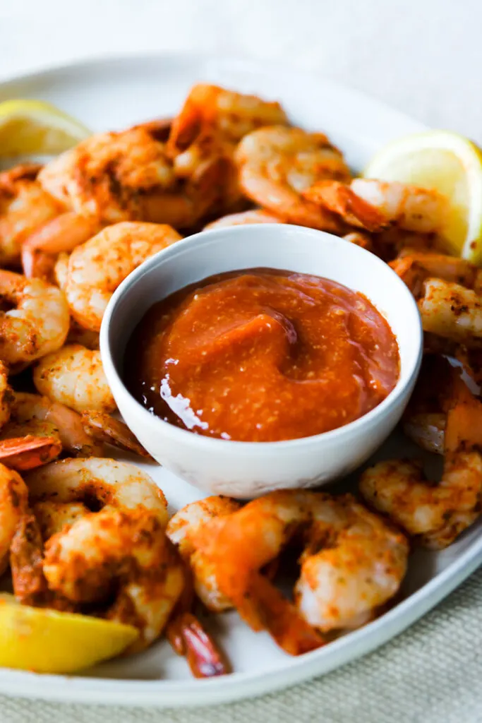 a small bowl of cocktail sauce on a plate of steamed shrimp and lemons