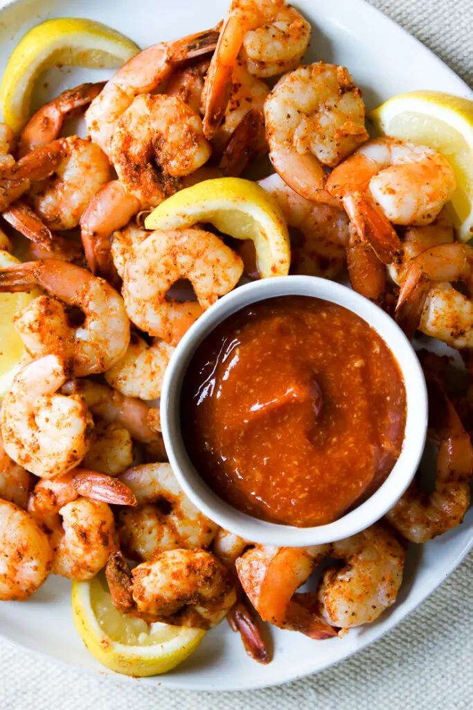 a bowl of cocktail sauce on a plate of squeezed lemons and steamed shrimp