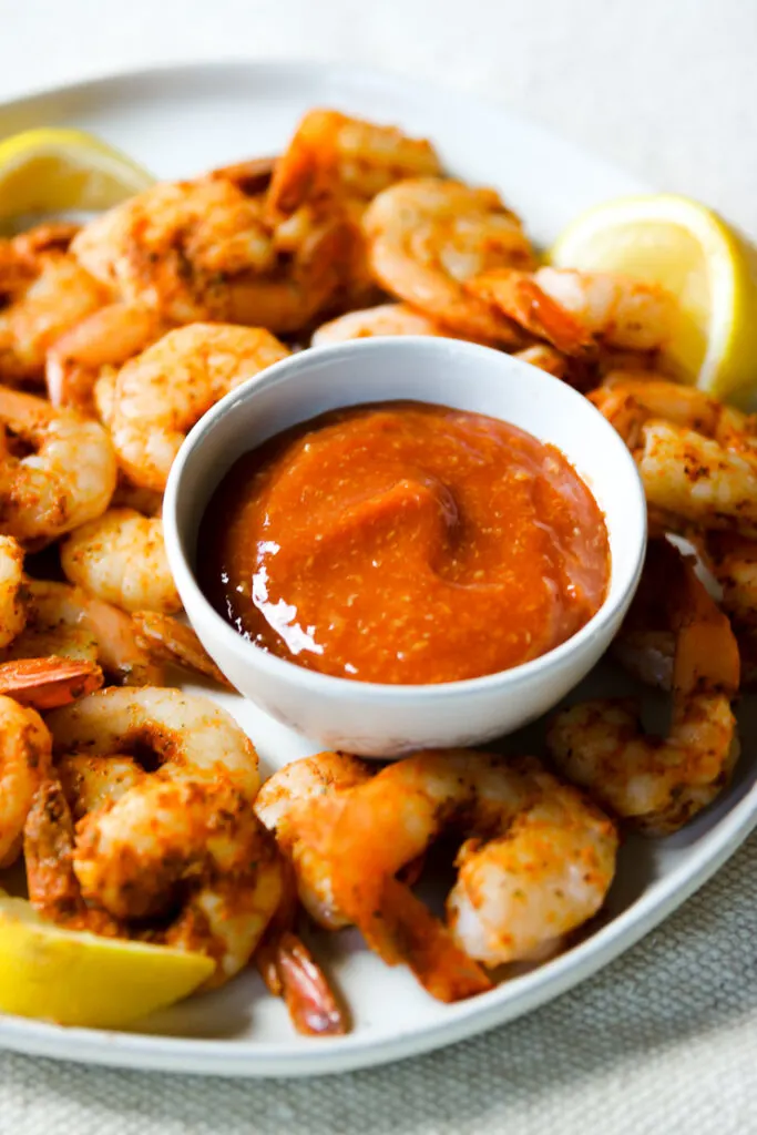 a bowl of cocktail sauce on a plate of steamed shrimp