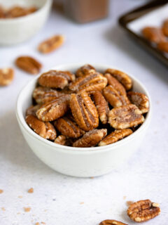 a small bowl of candied pecans with cinnamon and a cookie sheet in the background