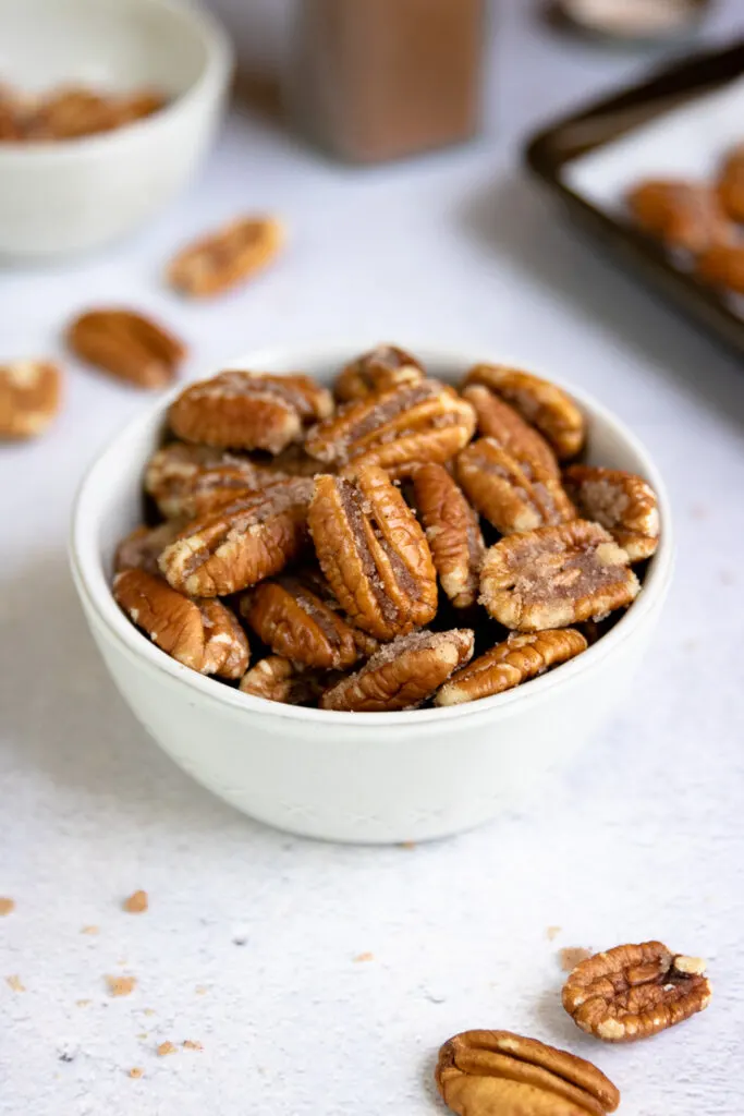 a small bowl of candied pecans with cinnamon and a cookie sheet in the background