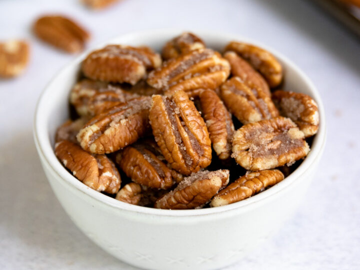 a small bowl of candied pecans with cinnamon and a cookie sheet in the background