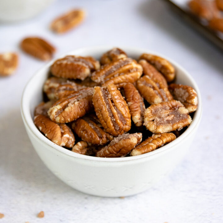 a small bowl of candied pecans with cinnamon and a cookie sheet in the background