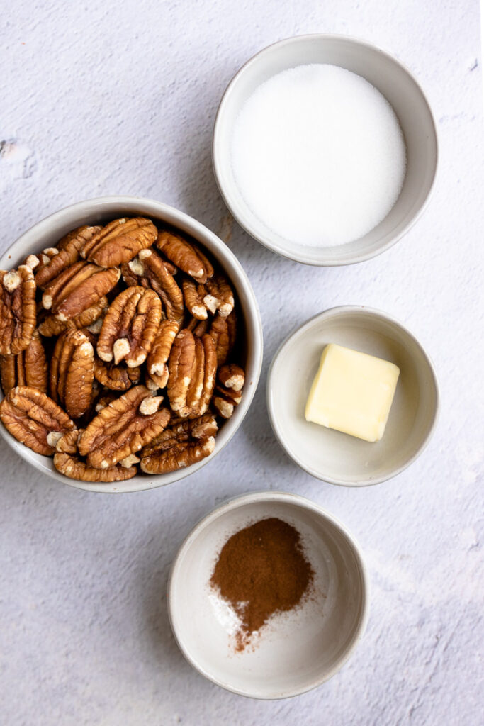 four white bowls with pecan halves, sugar, butter, and cinnamon