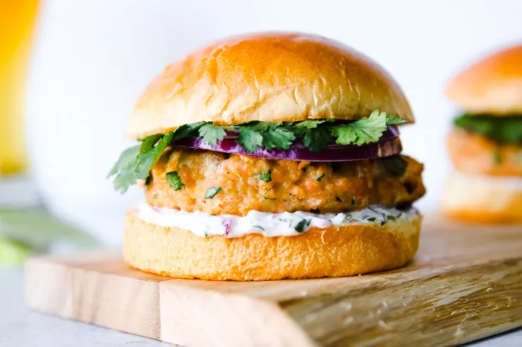 a brioche bun, with cilantro, red onion slices, salmon patty, and mayonnaise