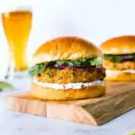 a grilled salmon burger on a wooden platter with a beer in the background