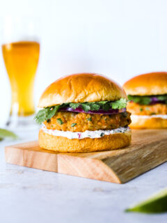 a grilled salmon burger on a wooden platter with a beer in the background