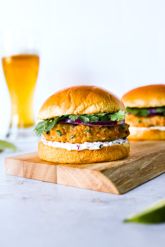 a grilled salmon burger on a wooden platter with a beer in the background