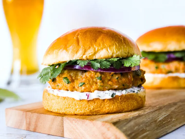 a grilled salmon burger on a wooden platter with a beer in the background