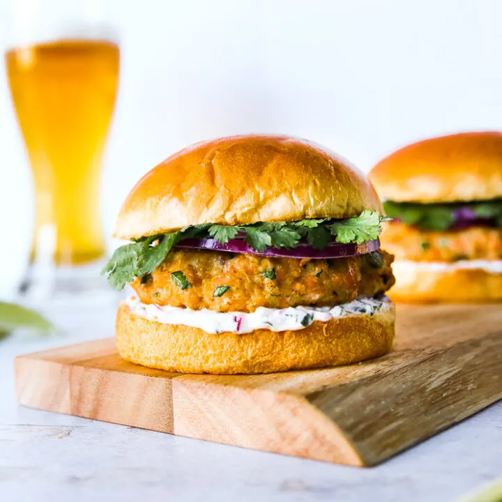 a grilled salmon burger on a wooden platter with a beer in the background