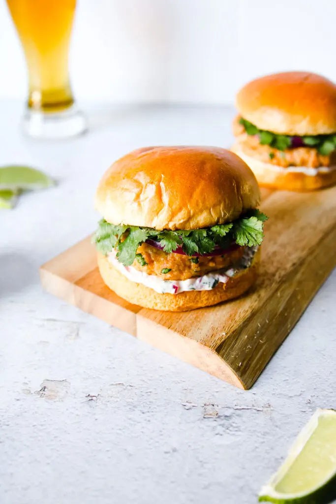 two grilled salmon burgers on a wood platter next to a beer