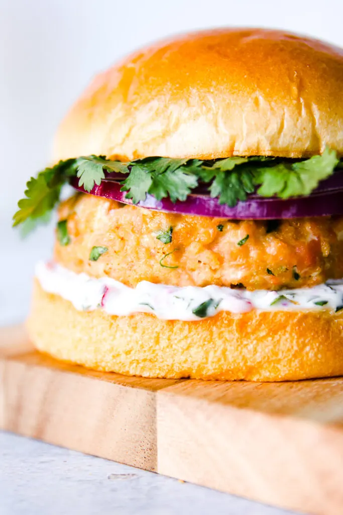 a close up of a grilled salmon burger on a wooden plank