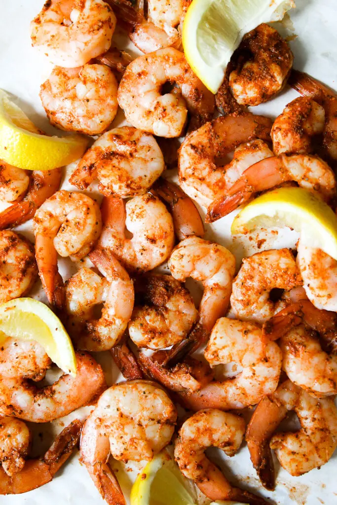 a pile of old bay steamed shrimp on parchment paper with lemon slices