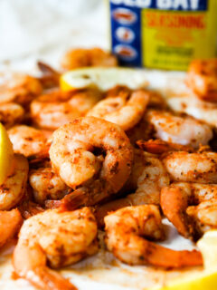 a pile of steamed shrimp, lemon slices, and container of old bay in the background