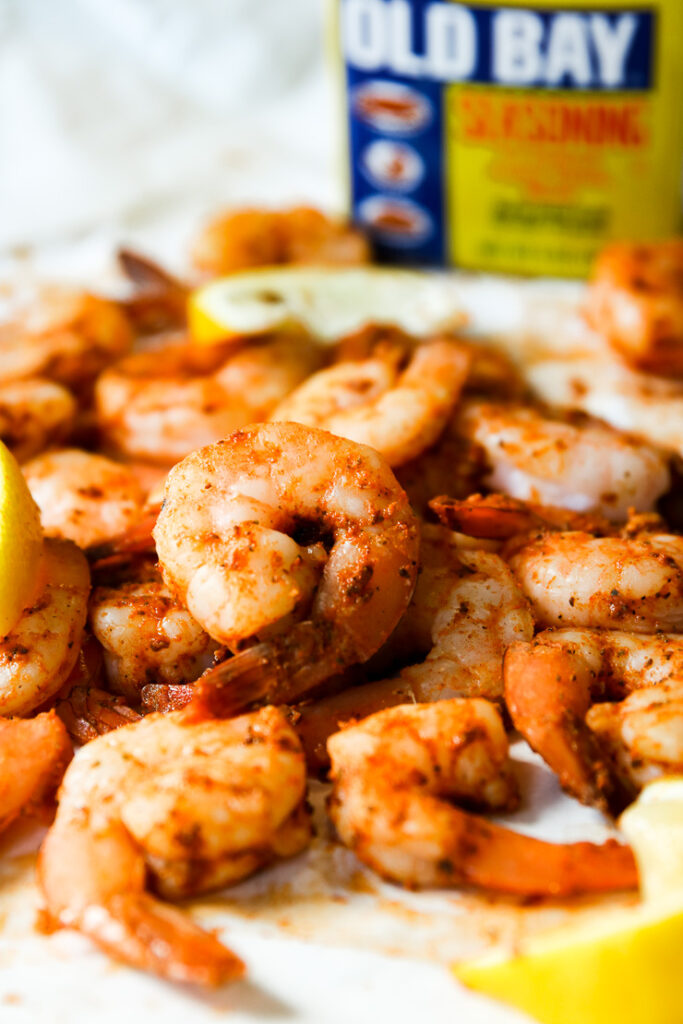 a pile of steamed shrimp, lemon slices, and container of old bay in the background