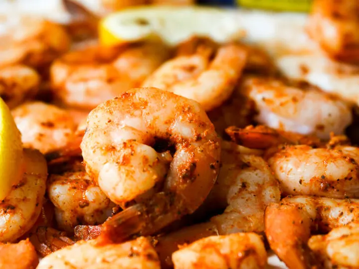 a pile of steamed shrimp, lemon slices, and container of old bay in the background