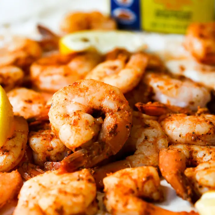 a pile of steamed shrimp, lemon slices, and container of old bay in the background