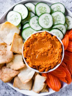 an overhead shot of roasted carrot hummus with veggies and pita chips on a plate