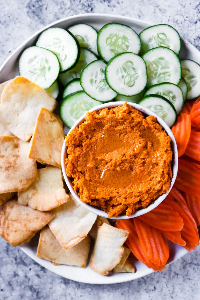 an overhead shot of roasted carrot hummus with veggies and pita chips on a plate