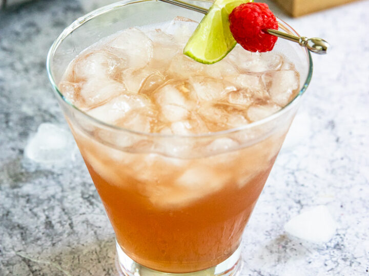 a pink chambord margarita filled with crushed ice and a metal pick with a lime slice and raspberry placed on top