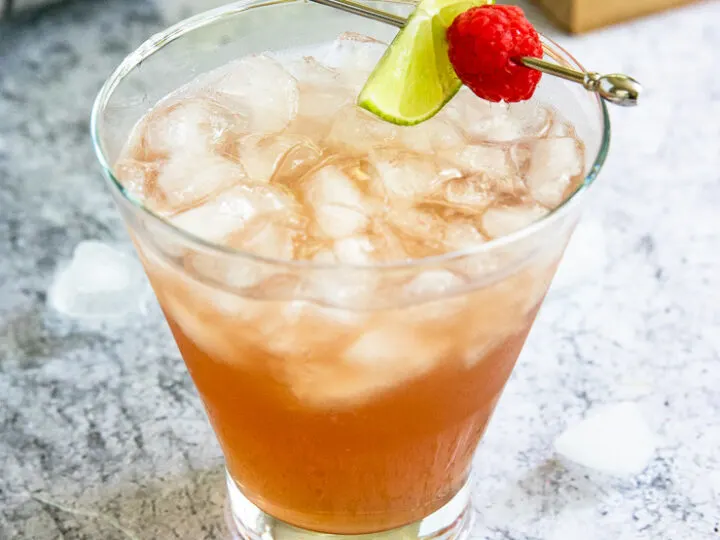 a pink chambord margarita filled with crushed ice and a metal pick with a lime slice and raspberry placed on top