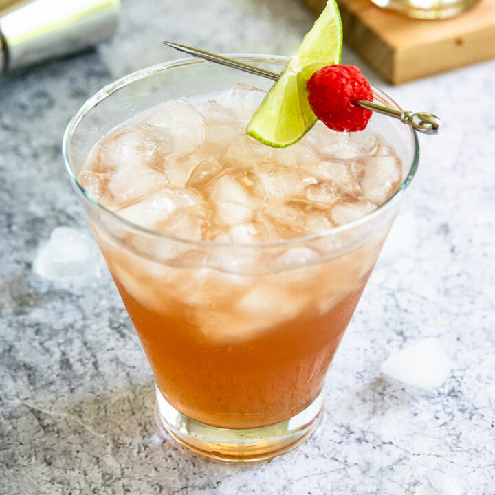 a pink chambord margarita filled with crushed ice and a metal pick with a lime slice and raspberry placed on top