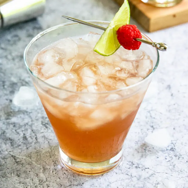 a pink chambord margarita filled with crushed ice and a metal pick with a lime slice and raspberry placed on top