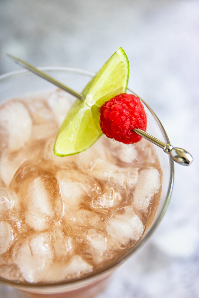 a close up of a metal pick with a lime slice and raspberry on the margarita glass