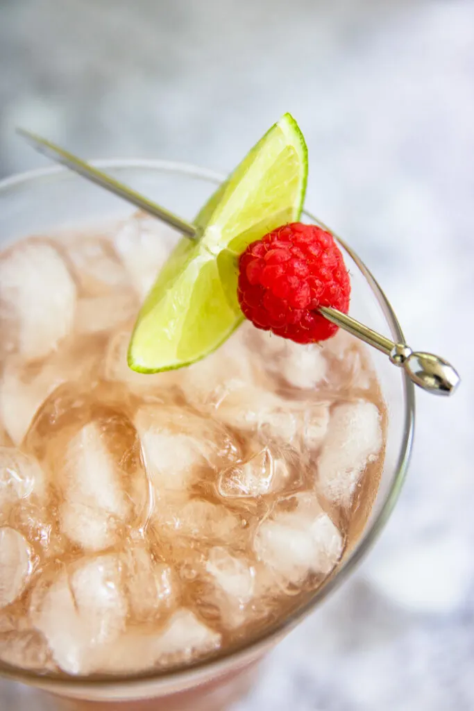 a close up of a metal pick with a lime slice and raspberry on the margarita glass