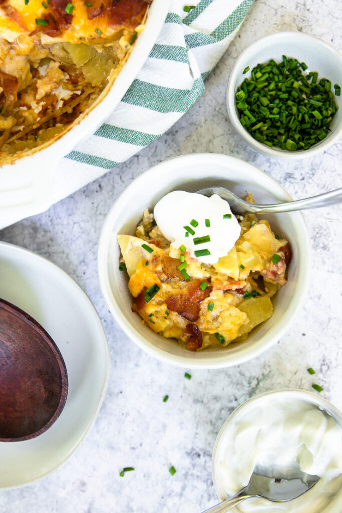 several white dishes that include diced chives, sour cream, loaded scalloped potatoes, and a serving with all three together