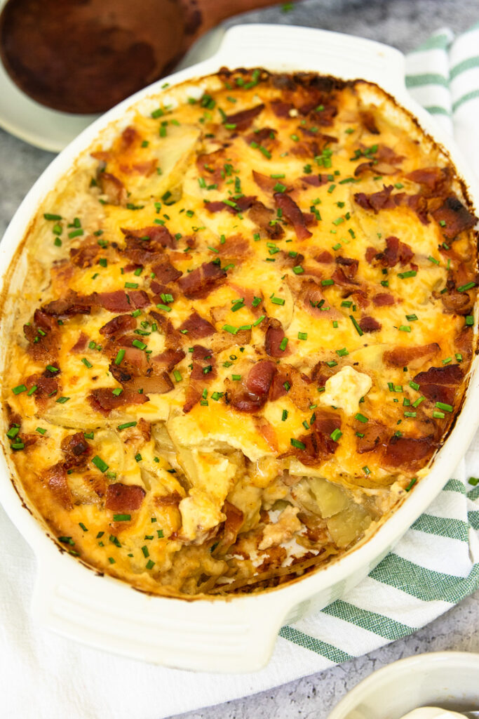 a scoop pulled out of the gratin dish of loaded scalloped potatoes with a wooden spoon in the background