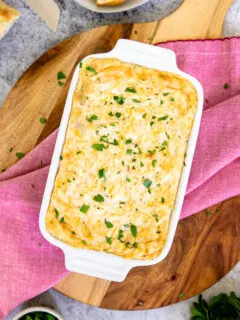 a baking dish with baked maryland crab dip and diced parsley on top of a red napkin and wooden cutting board