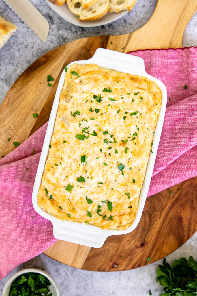 a baking dish with baked maryland crab dip and diced parsley on top of a red napkin and wooden cutting board